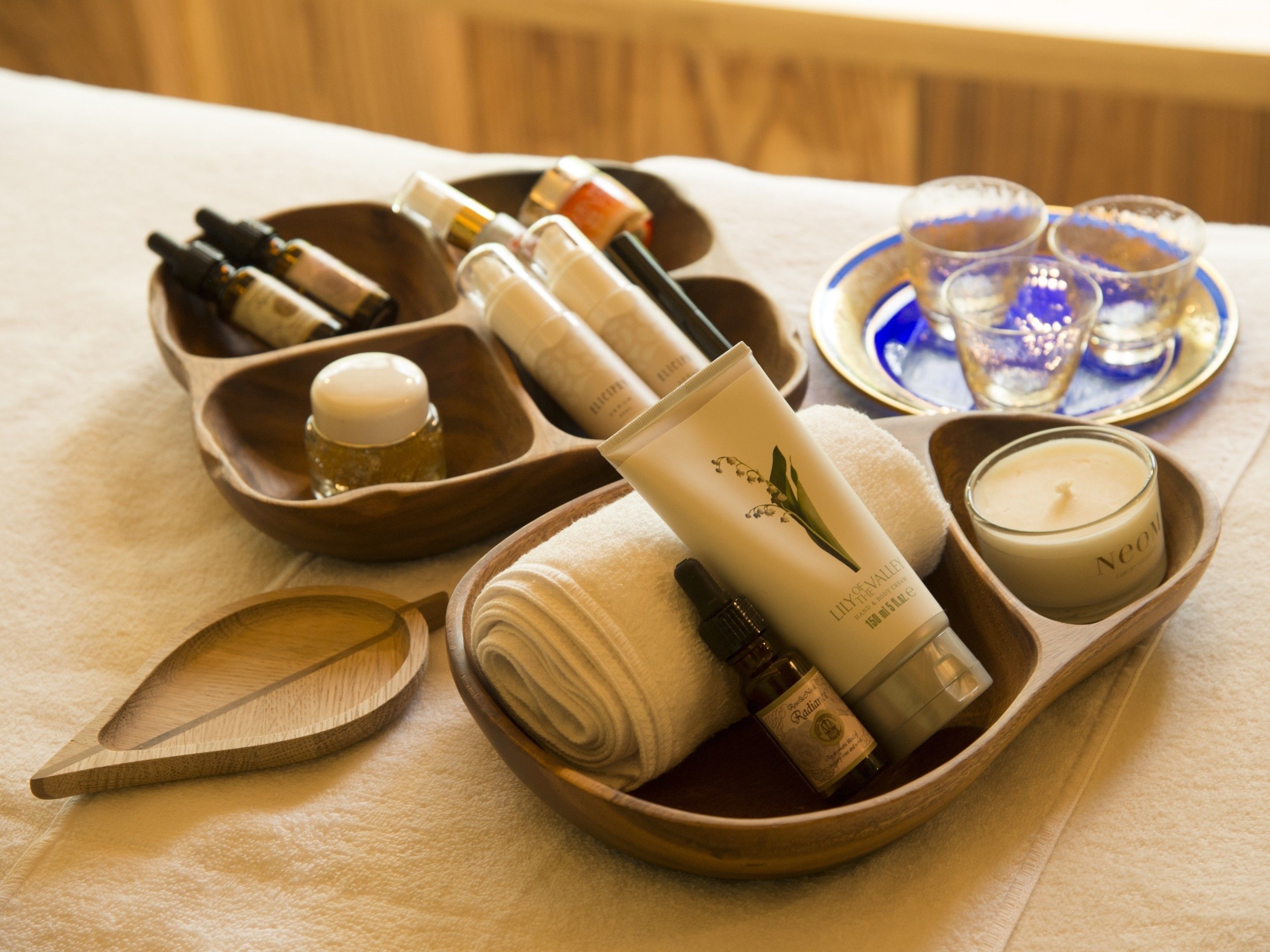 A wooden tray with various toiletries and a candle, placed on a table with a towel and a wooden spoon.