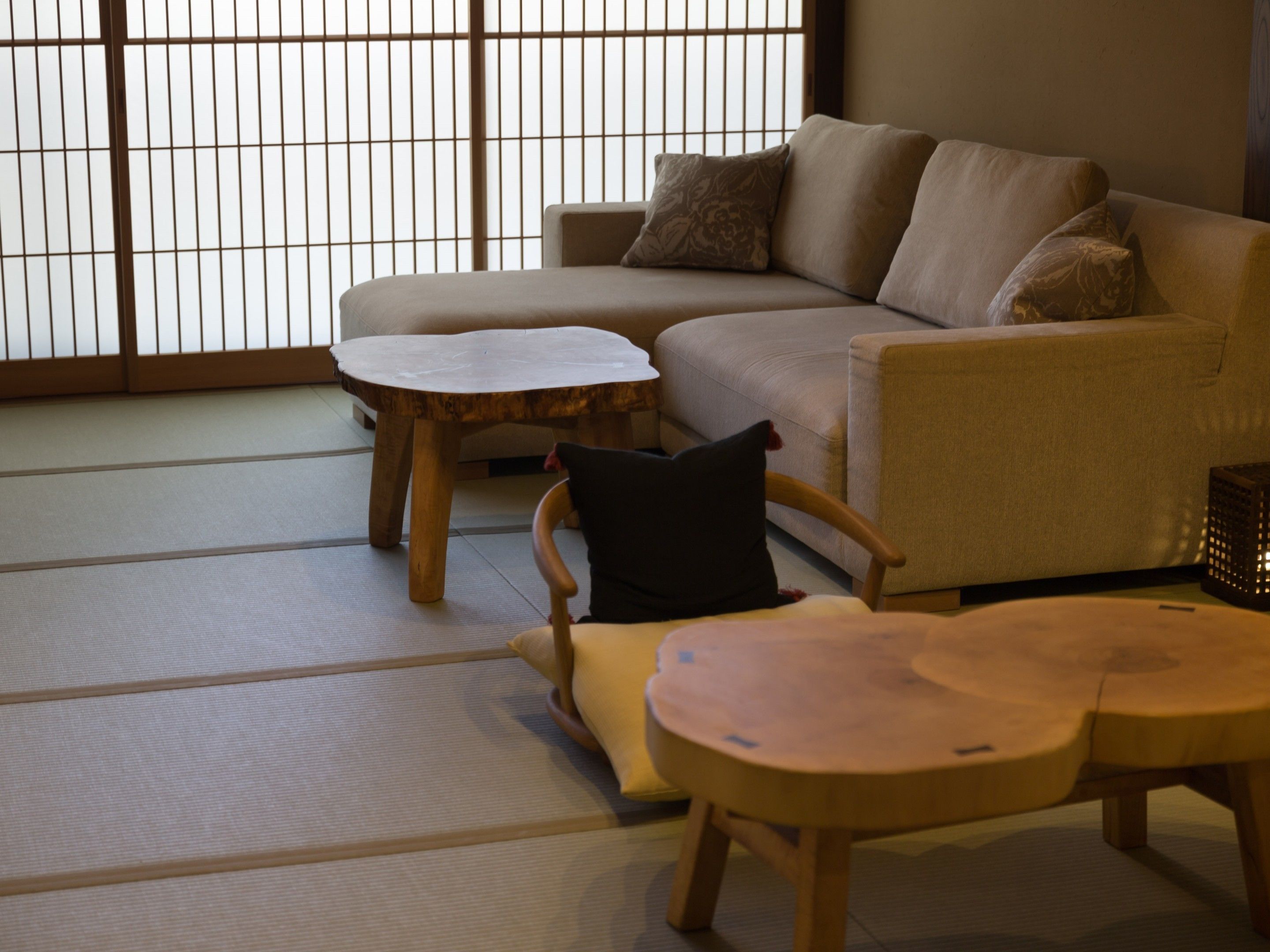 Um quarto em estilo japonês tradicional, com tatames, uma mesa de madeira baixa, um sofá e uma poltrona acolchoada.