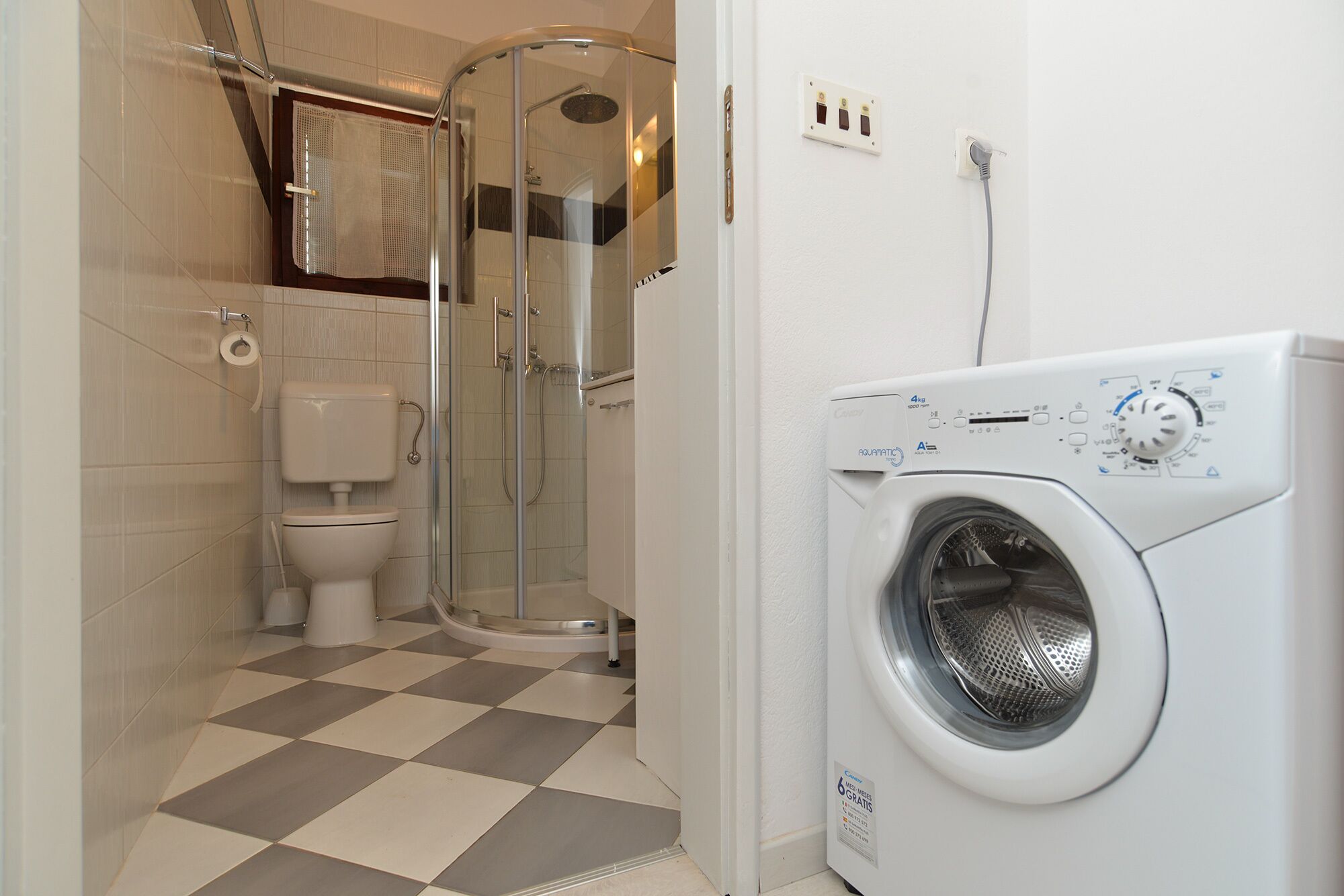 A bathroom with a shower, toilet, and a front-loading washing machine.