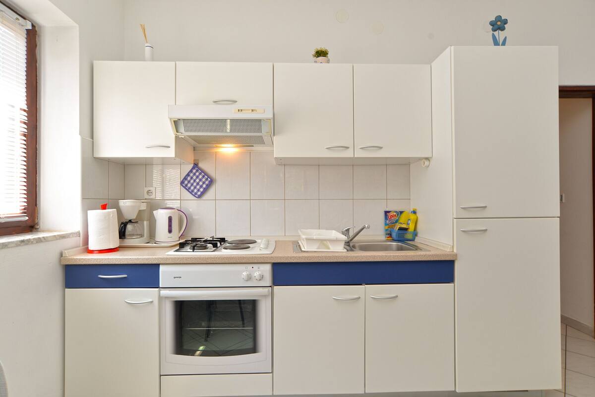 Een kleine keuken met witte kastjes, een gasfornuis, een inbouwoven en een spoelbak.