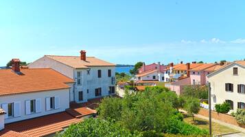 A coastal village with terracotta-roofed buildings, a clear blue sky, and a view of the sea.