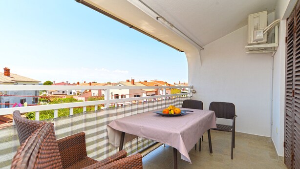 Un balcon agrémenté de meubles en osier, une table avec un panier de fruits et une vue sur les immebles.