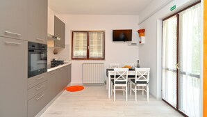 Une cuisine moderne avec des meubles gris, un four encastré et un coin repas comprenant une table et des chaises blanches.