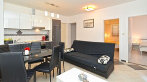 Un salon moderne avec un canapé noir, une table à manger avec des chaises et un coin cuisine doté de meubles blancs et d’une cuisinière.