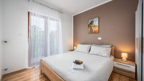 A neatly made bed with a white and grey striped bedspread, a small bedside table with a lamp, and a painting on the wall. - Apartment Klaudio 294 (Rasa)