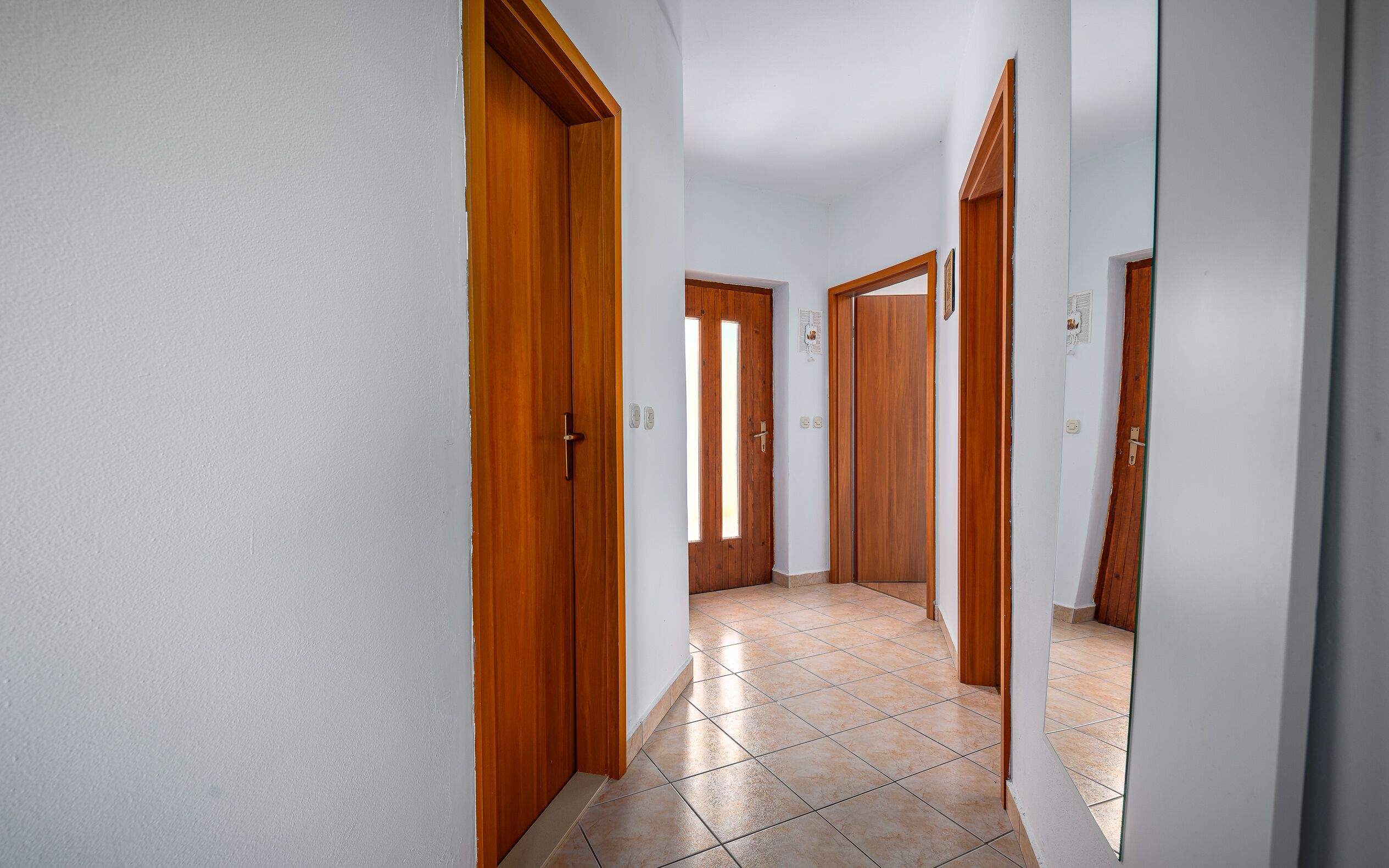 Un pasillo con puertas de madera y suelo de baldosas.