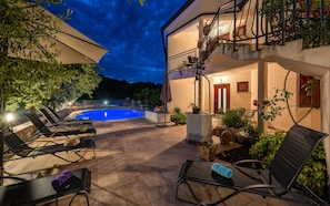 A poolside area with lounge chairs, a small table, and potted plants.