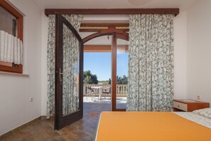 A bedroom with a bed, a wooden nightstand, and a view of an outdoor patio with a table and chairs. - Apartment Milorad 324 (Medulin)