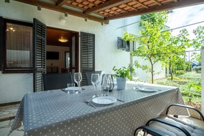An outdoor dining area with a table set for two, a potted plant, and a view of a garden. - Apartment Jan 325 (Medulin)