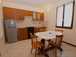 A compact kitchen with wooden cabinets, a stainless steel refrigerator, a stove, and a dining table with four wooden chairs. - Apartment Jan 325 (Medulin)