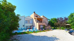 Ein zweistöckiges Gebäude mit Balkon, Poolbereich mit Liegestühlen und einer Schotterauffahrt.