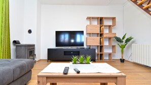 Ein modernes Wohnzimmer mit Flachbildfernseher, Couchtisch aus Holz, grauem Sofa und einer Holzregaleinheit.
