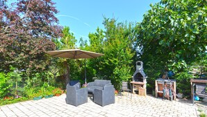 Eine Terrassengaststätte mit Korbmöbeln, einem Grill und einer Pergola mit Sonnenschirm.