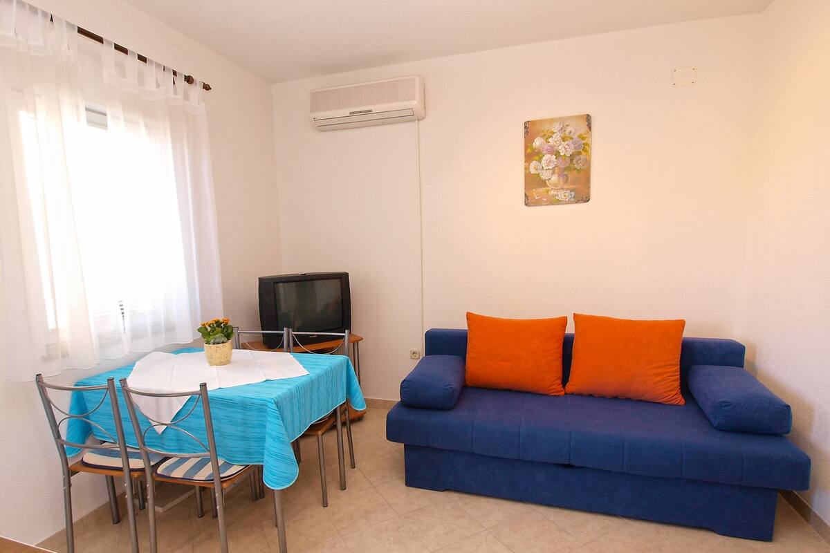 A living room with a blue sofa, a dining table with chairs, a television, and a painting on the wall.