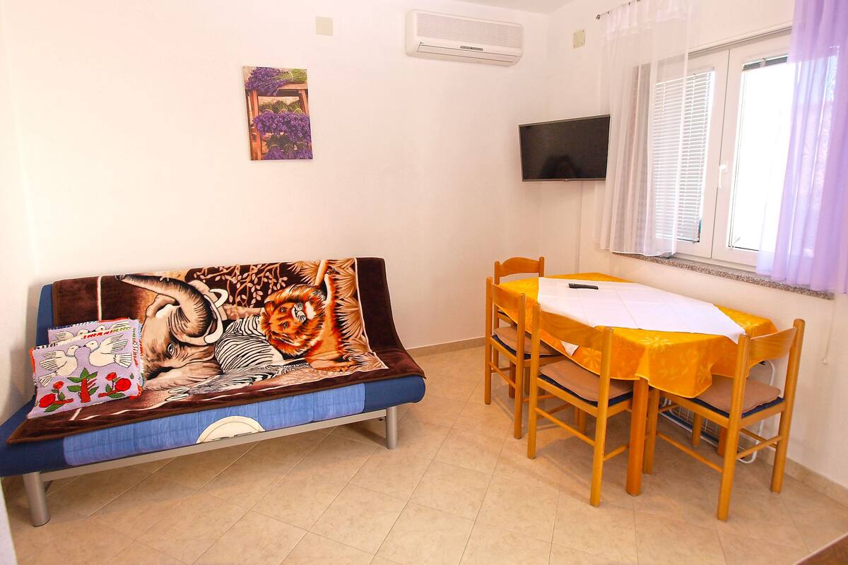 A small room with a sofa, a table, chairs, a TV, and a window with curtains.