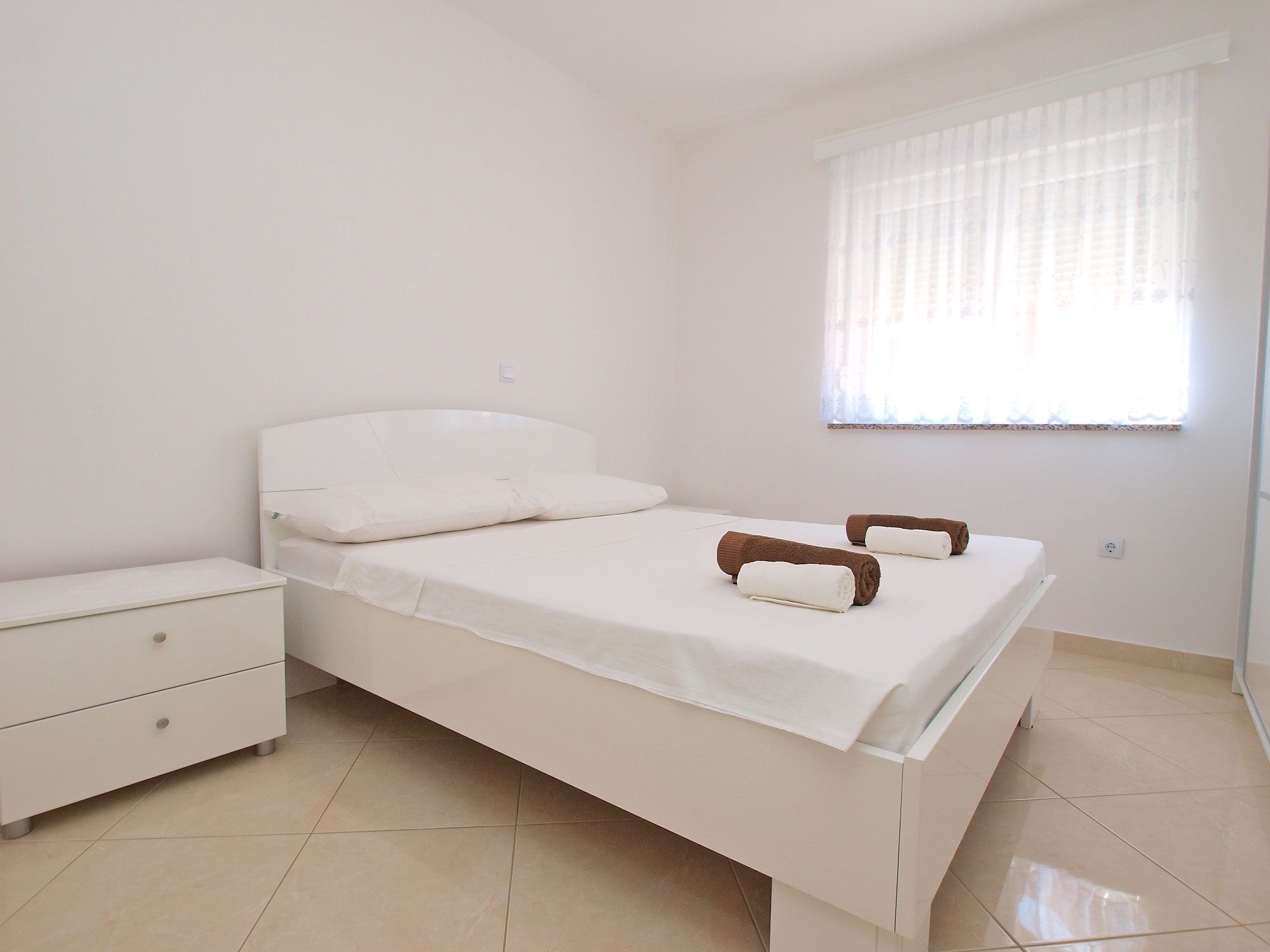 A minimalist bedroom with a bed, a nightstand, and a window with sheer curtains.