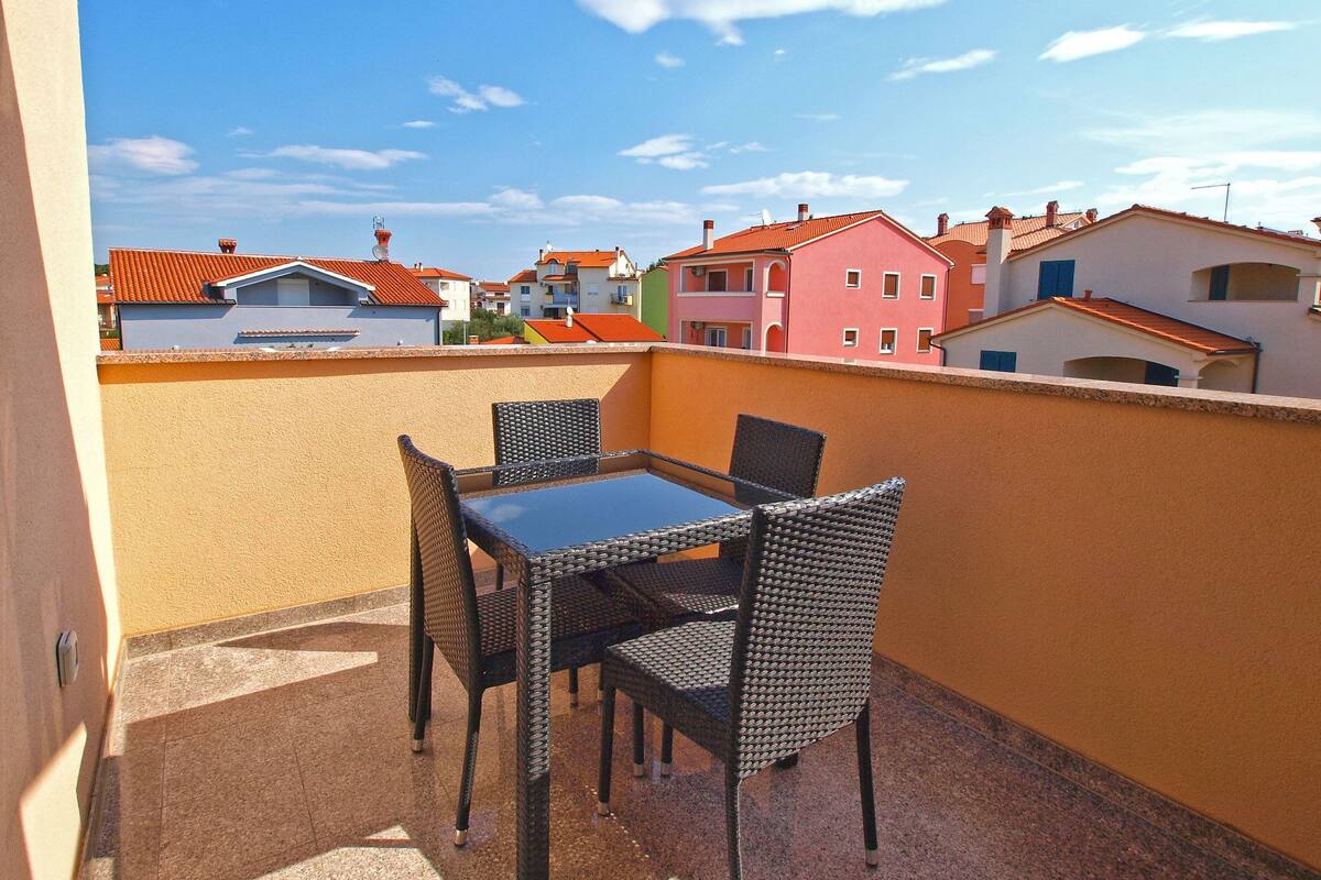 Un balcón con mesa y sillas, con vistas a edificios coloridos de techos rojos y anaranjados.
