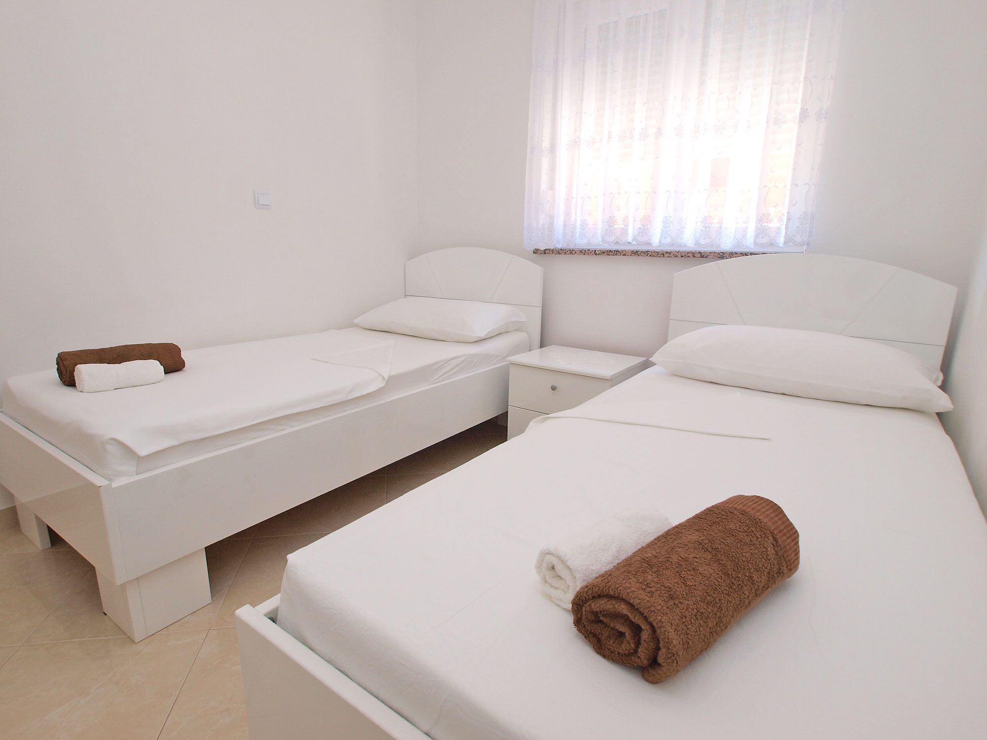 A twin room with two single beds, a nightstand, and a window with sheer curtains.