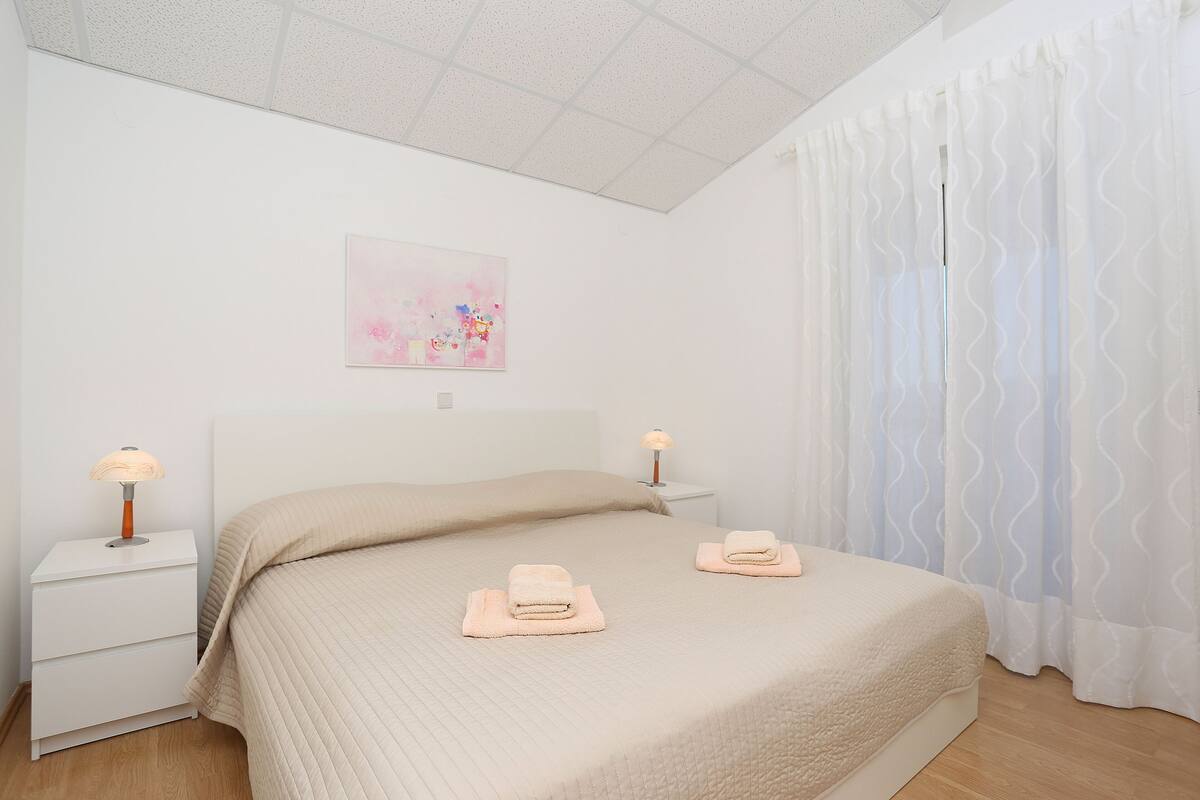 Een slaapkamer met een bed, twee nachtkastjes, een wandlamp en een raam met gordijnen.
