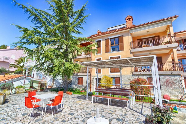 A two-story building with a stone patio, outdoor seating, and a pergola.