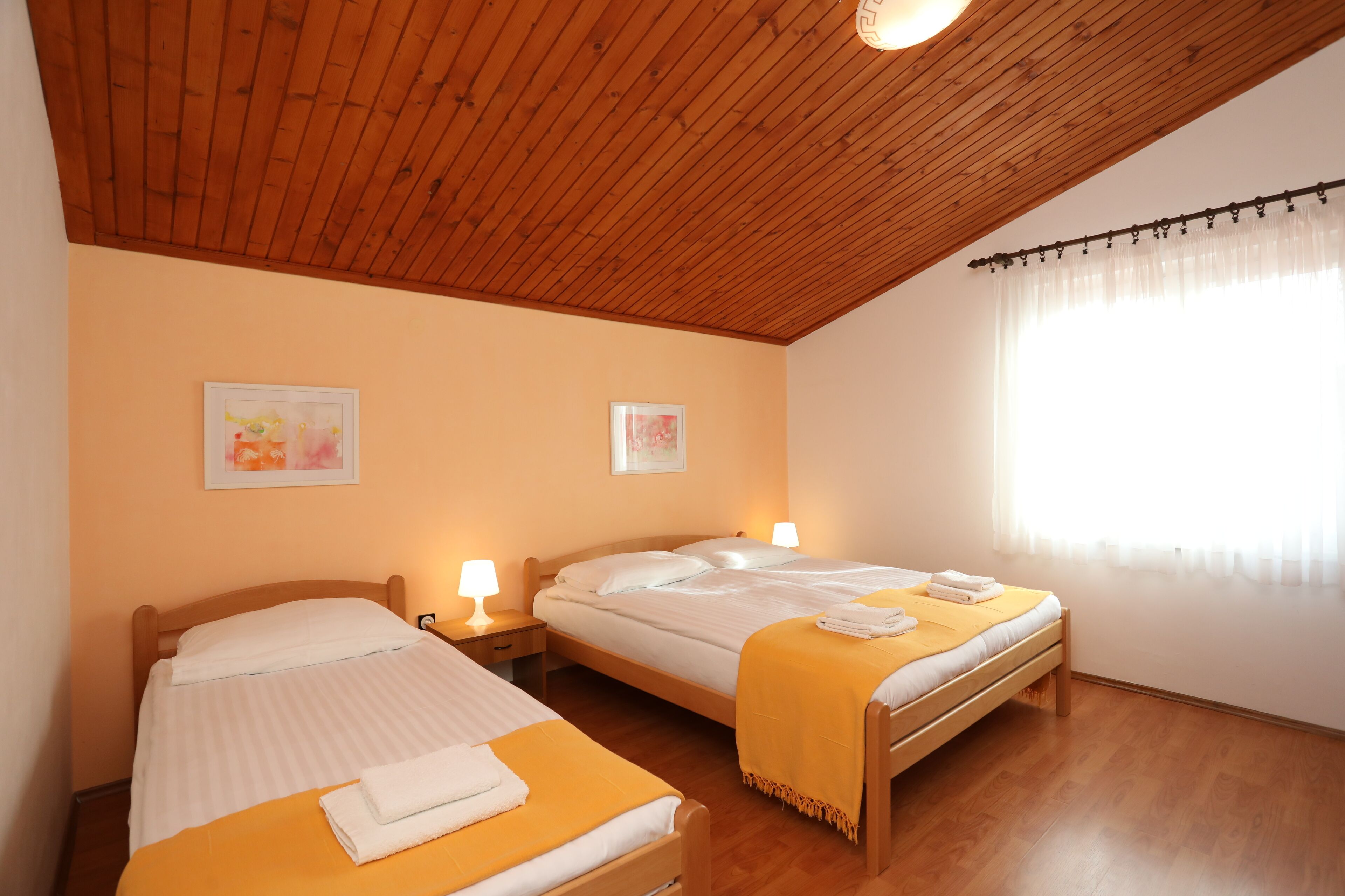 Une chambre avec deux lits, un plafond en bois et une fenêtre ornée de rideaux légers.