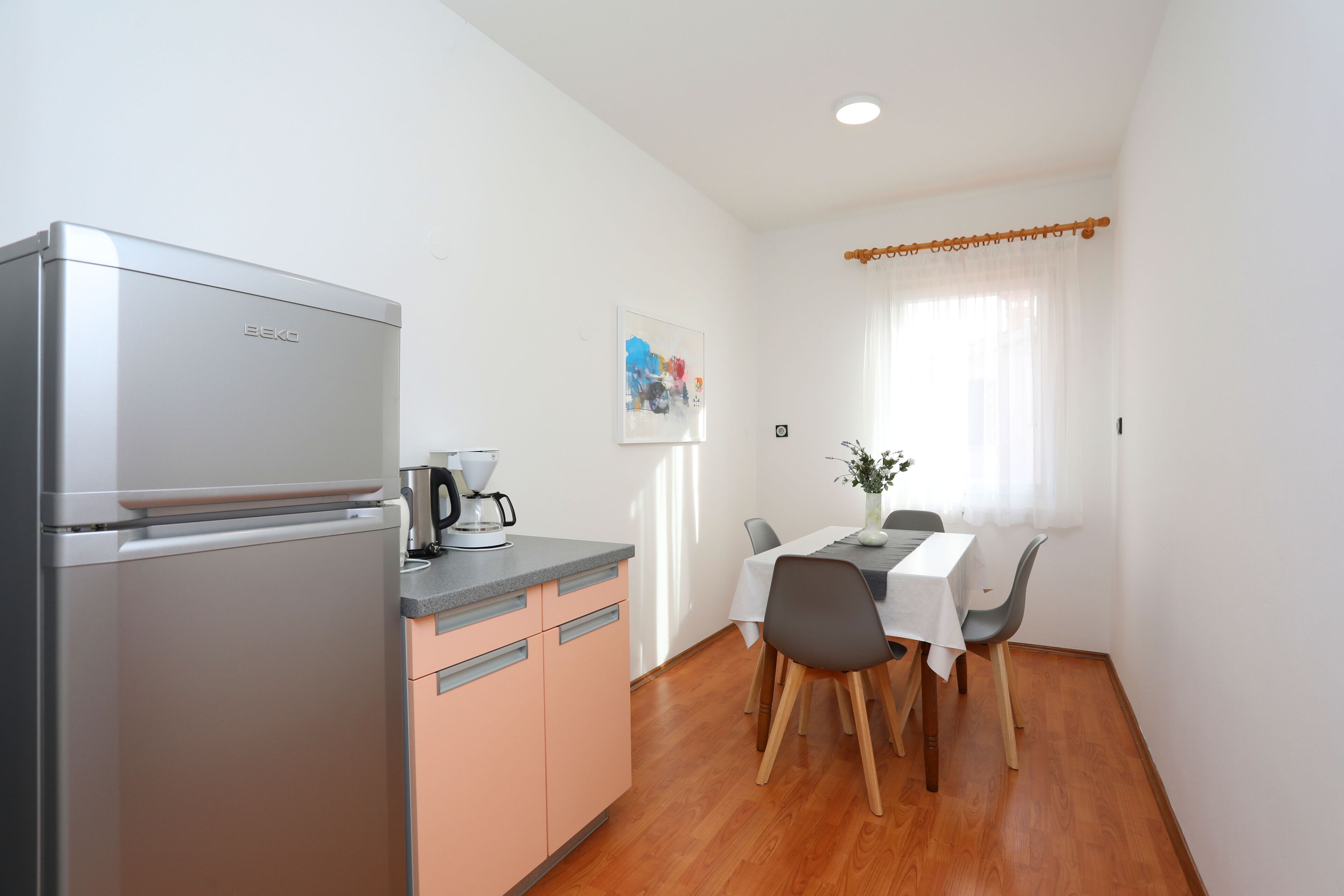 Una cocina compacta con refrigerador, cafetera y una mesa de comedor con sillas.