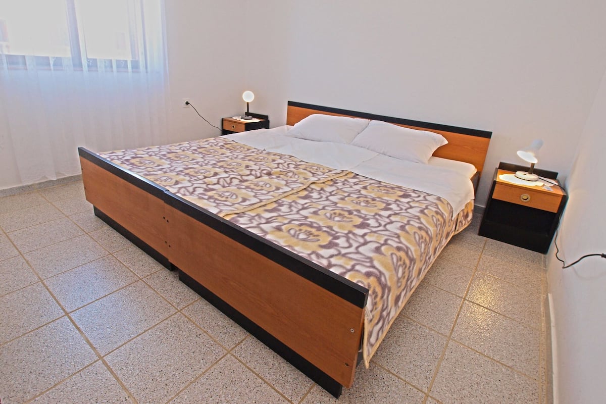 A bedroom with a wooden bed, white bedding, two bedside tables with lamps, and a window with curtains.