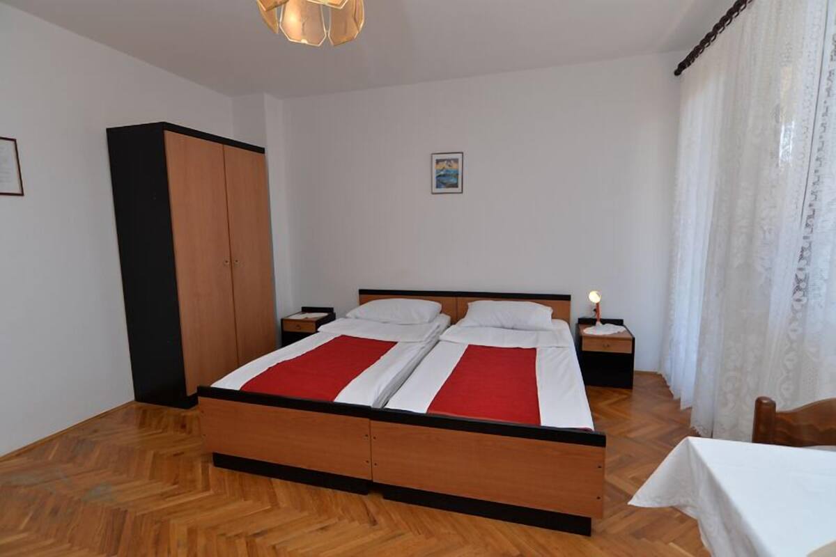 A double bed with a red and white bedspread, wooden headboard, two bedside tables with lamps, a wardrobe, and a painting on the wall.