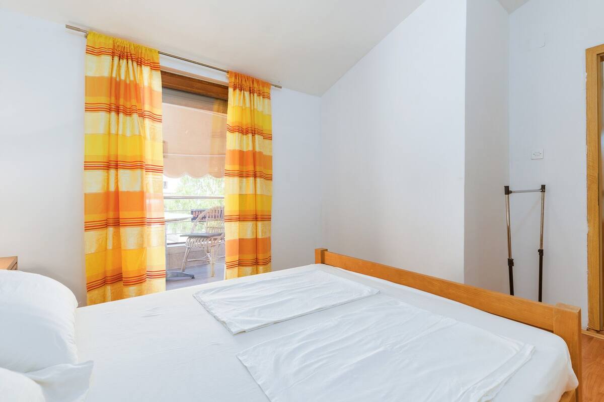 A bedroom with a bed, a window with curtains, a wooden headboard, and a door.
