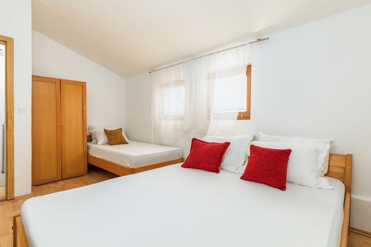 A bedroom with a large bed, two single beds, a wooden wardrobe, and a window with sheer curtains.