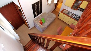 Una escalera conduce a una sala de estar con sofá, cocina y mesa de comedor.