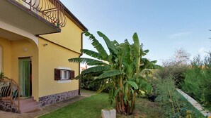 Un edificio amarillo con base de piedra, una ventana pequeña con contraventanas y una puerta verde.