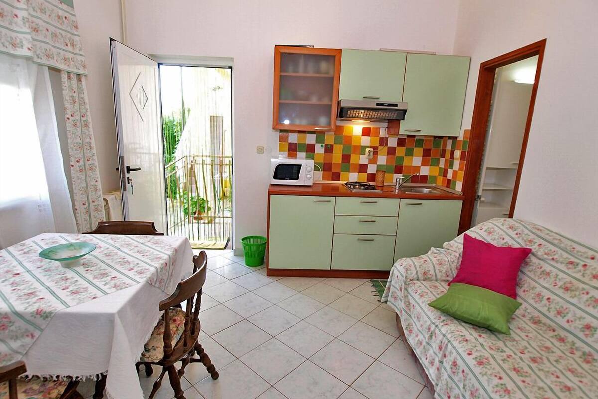 A compact living space with a dining table, a sofa, a kitchenette, and a sliding glass door leading to a balcony.