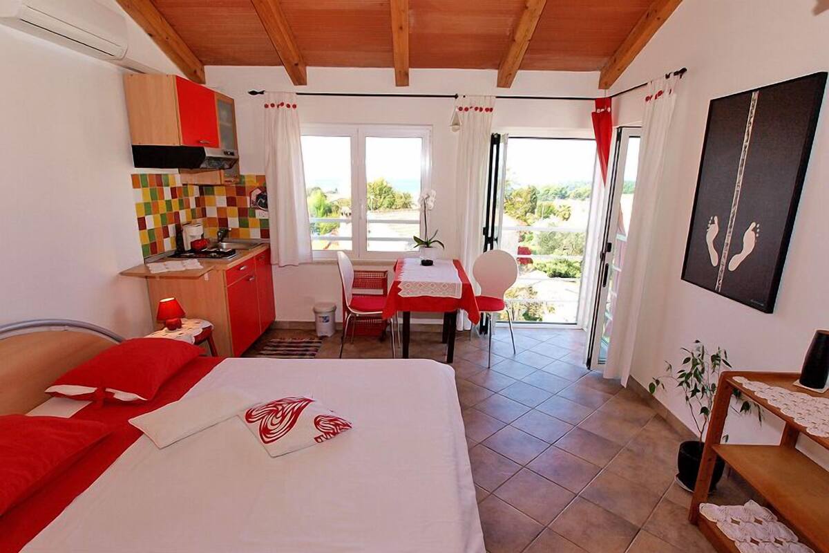 A bedroom with a bed, a small kitchenette, and a dining area with a table and chairs.