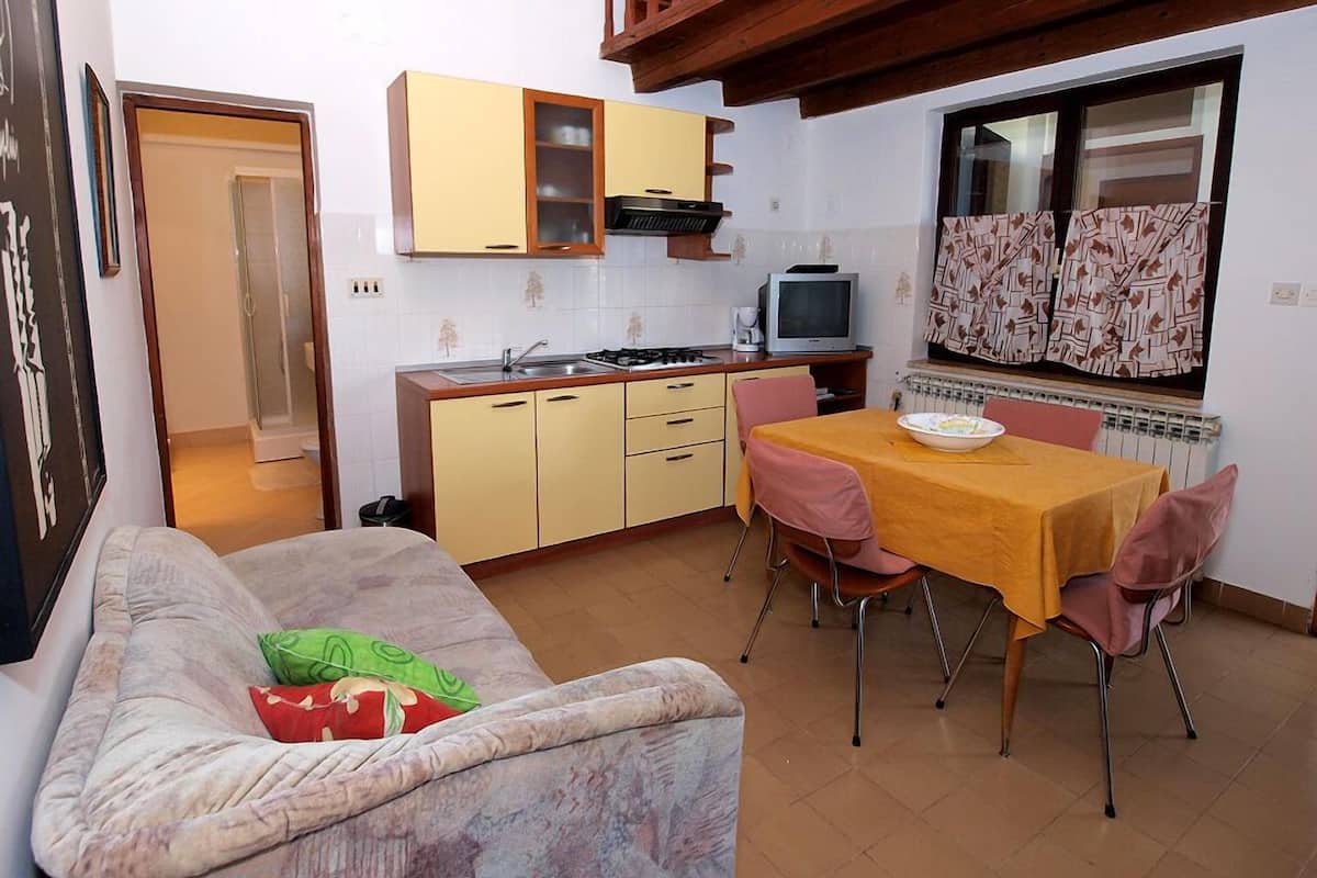 A compact living space with a kitchenette, a sofa, a dining table with chairs, and a window with curtains.