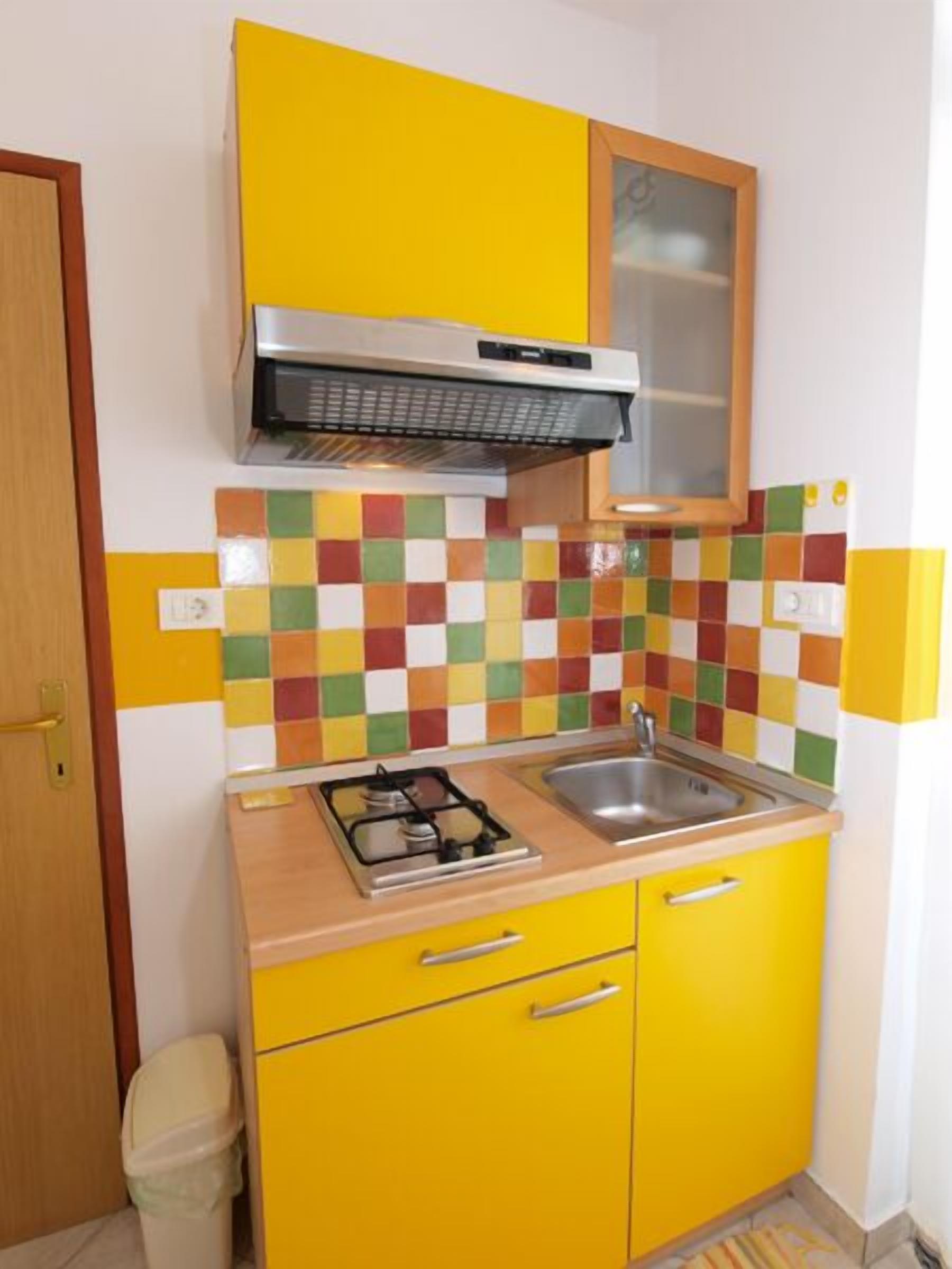 A compact kitchen with yellow cabinets, a gas stove, a sink, and a colorful tile backsplash.