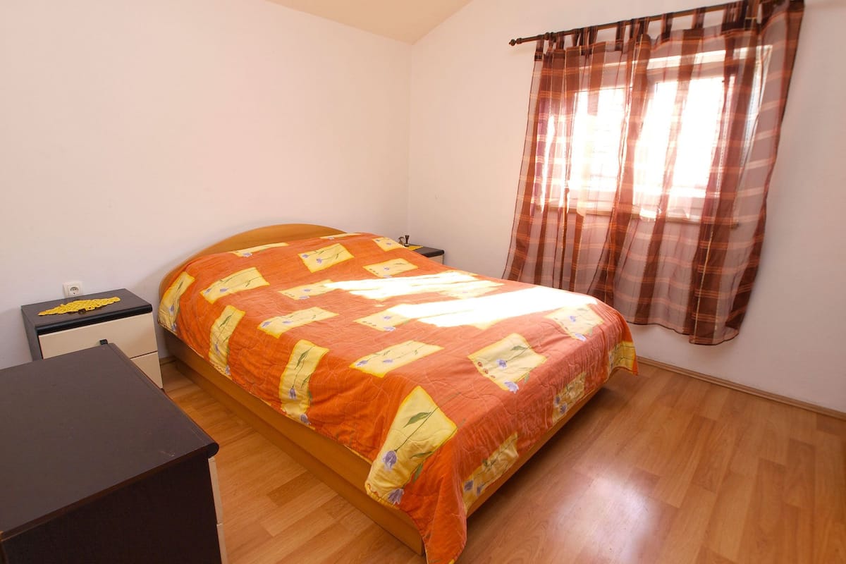 Une chambre à coucher comprenant un lit, une table de chevet, une commode et une fenêtre avec des rideaux.