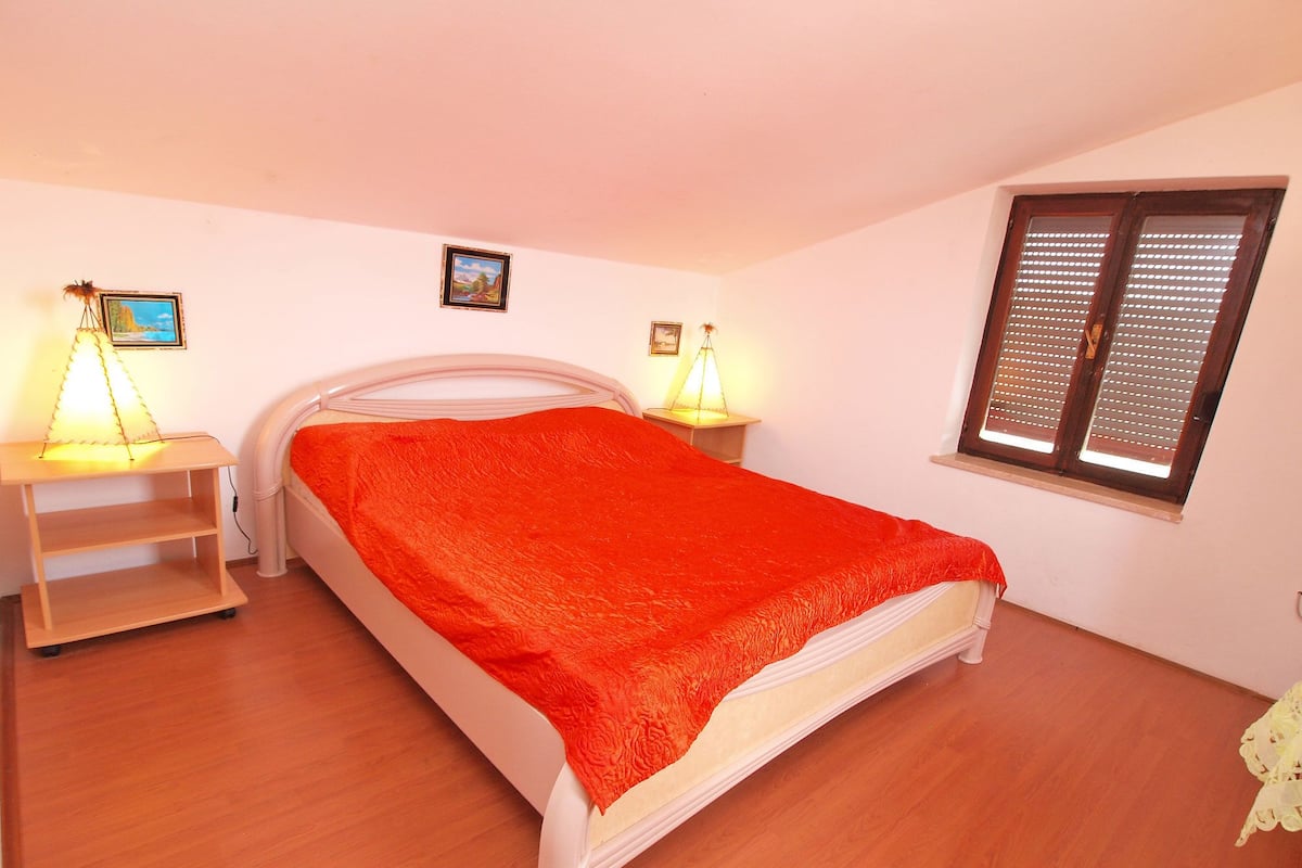 Une chambre à coucher comprenant un lit, deux tables de chevet, une fenêtre et un tableau accroché au mur.