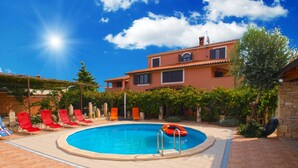 Una piscina con sillas de descanso rojas, un flotador salvavidas y un edificio de piedra al fondo.