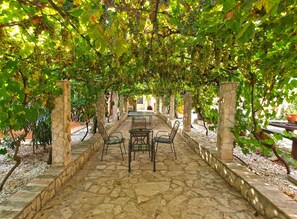 An outdoor covered patio with stone flooring, a table with chairs, and a pergola with grapevines overhead. - Apartment Franko 749 (Pula)