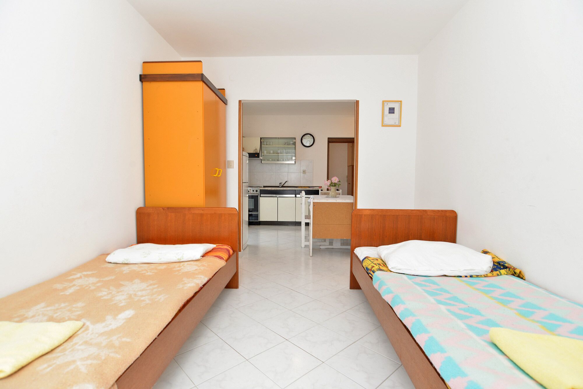 A room with two single beds, a kitchenette, and a bathroom visible through an open door.