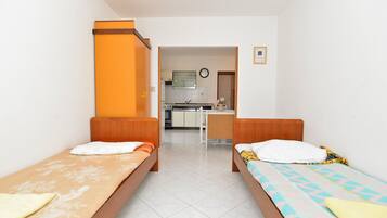 A room with two single beds, a kitchenette, and a bathroom visible through an open door.