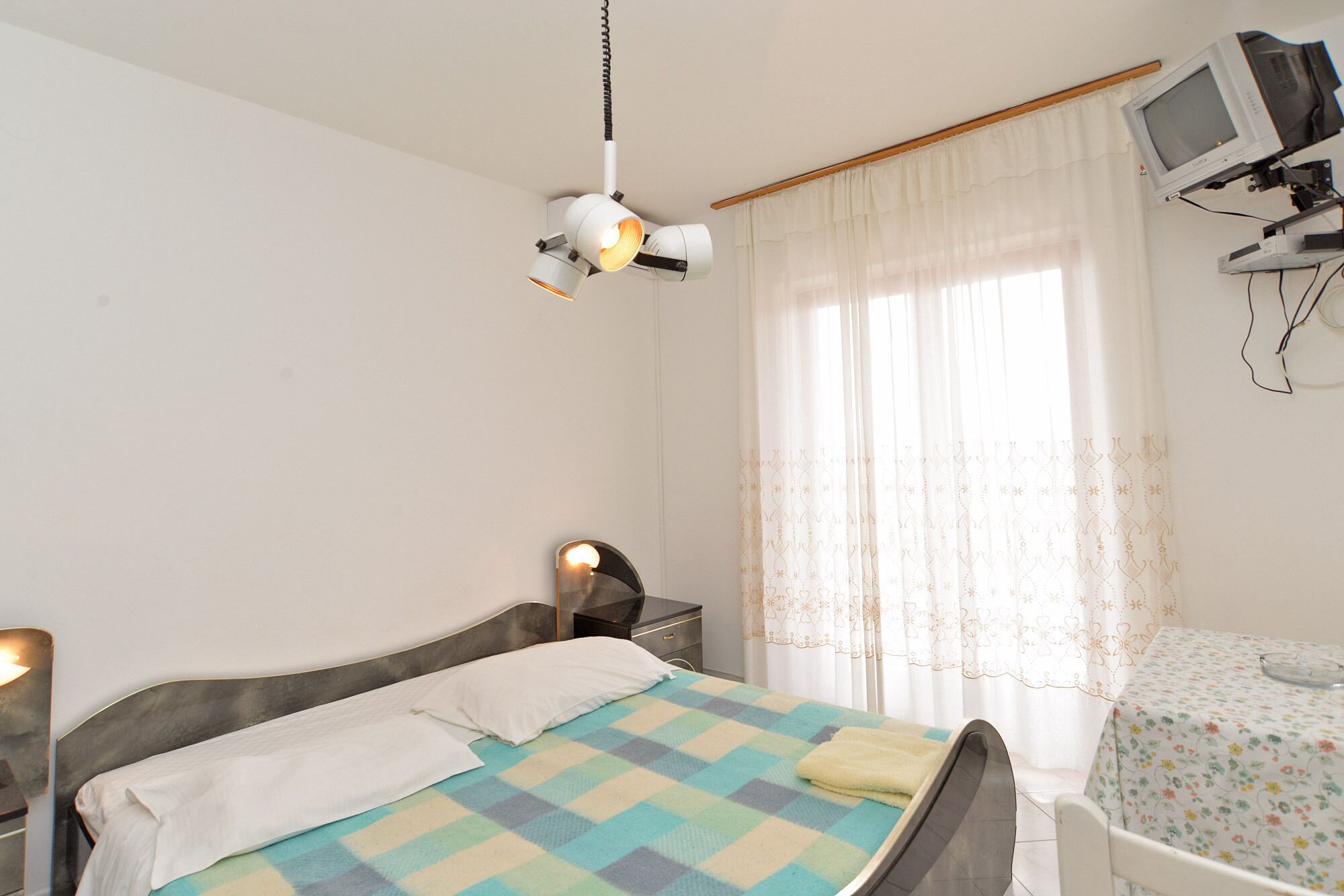 A bedroom with a bed, a desk, a chair, a television, and a ceiling light.