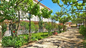 A garden pathway leading to a building with a red roof, surrounded by greenery and potted plants. - Apartment Aleksander 968 (Fazana)