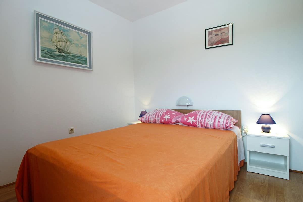 A bedroom with a bed, a nightstand, a lamp, and two framed pictures on the wall.