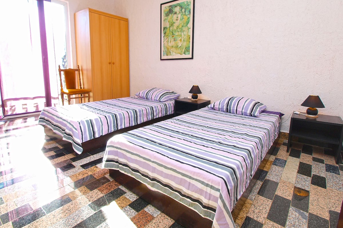 A hotel room with two beds, a wardrobe, a chair, and a painting on the wall.