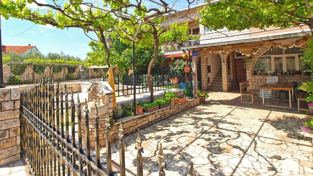 A courtyard with a stone floor, a pergola with grapevines, a stone wall, and a small outdoor seating area with a table and chairs. - Apartment Aleksander 968 (Fazana)