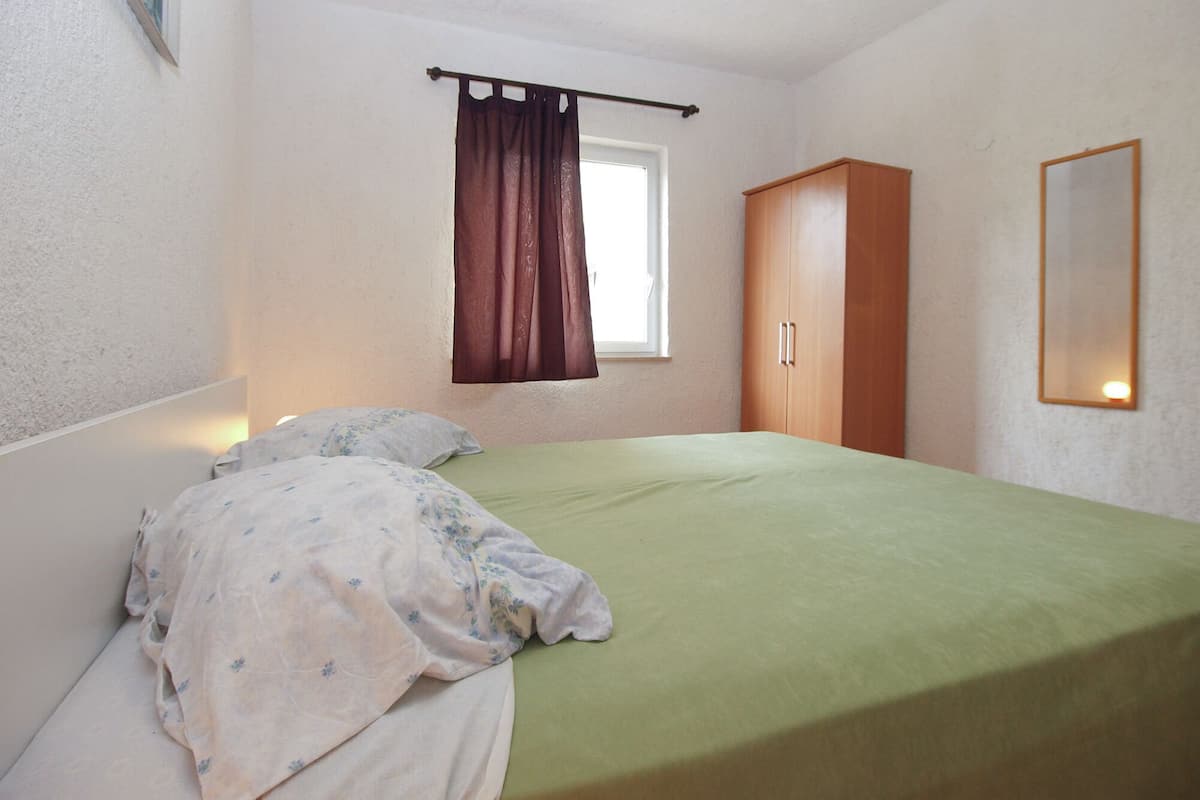 A bedroom with a bed, a window with curtains, a wardrobe, and a mirror.