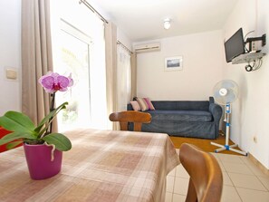 Una habitació amb taula de menjador, sofà, televisió penjada a la paret i finestra amb cortines.