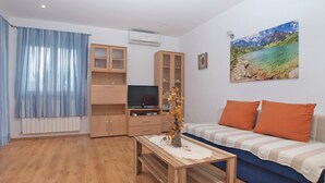 A living room with a sofa, a TV, wooden cabinets, and a painting of a landscape. - Apartment Mirsad 1282 (Fazana)